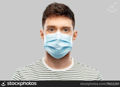 health protection, safety and pandemic concept - young man in protective medical mask over grey background. young man in protective medical mask