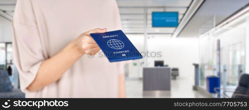 health protection, vaccination and pandemic concept - close up of woman holding immunity passport over airport background. close up of woman holding immunity passport