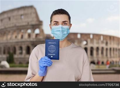 health protection, vaccination and pandemic concept - close up of young woman in medical mask and gloves holding immunity passport over colosseum in rome, italy on background. woman in mask and gloves holding immunity passport