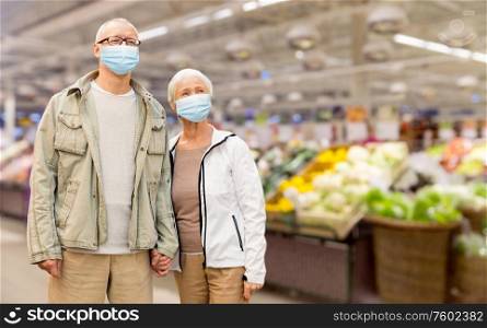 health, quarantine and pandemic concept - senior couple wearing protective medical mask for protection from virus holding hands over supermarket on background. senior couple in medical masks at supermarket