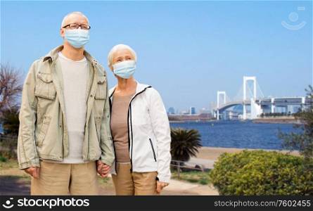 health, quarantine and pandemic concept - senior couple wearing protective medical mask for protection from virus holding hands over tokyo city, japan background. senior couple in protective medical masks in japan