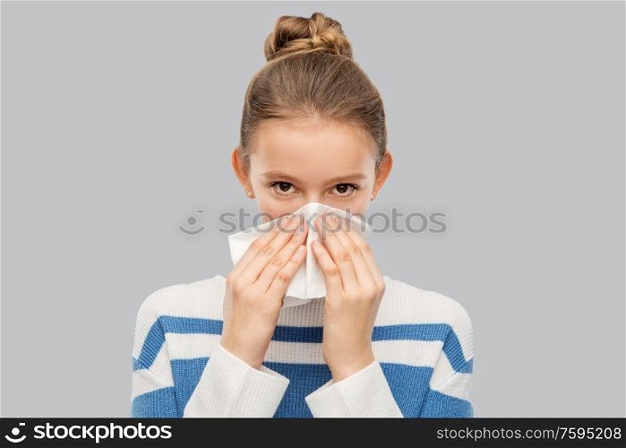 health, rhinitis and people concept - sick teenage girl blowing runny nose with paper tissue over grey background. sick teenage girl blowing nose with paper tissue