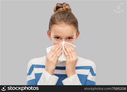 health, rhinitis and people concept - sick teenage girl blowing runny nose with paper tissue over grey background. sick teenage girl blowing nose with paper tissue