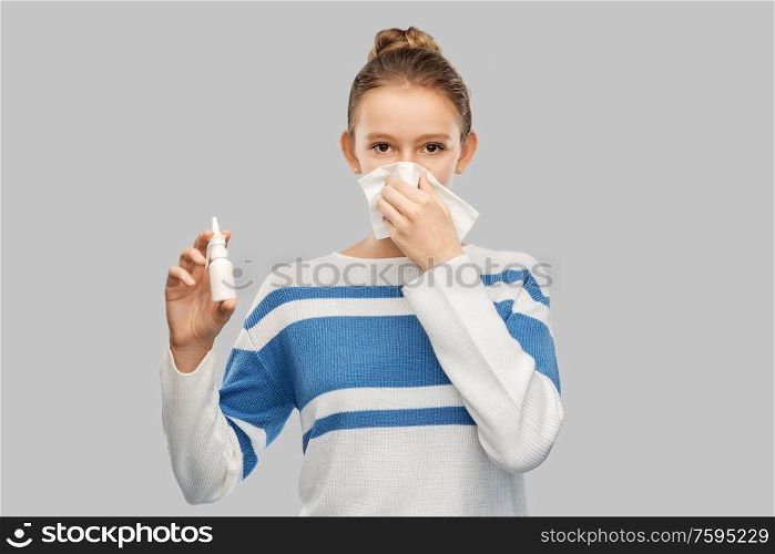 health, rhinitis and people concept - sick teenage girl blowing runny nose with paper tissue and using nasal spray over grey background. sick teenage girl with nasal spray blowing nose