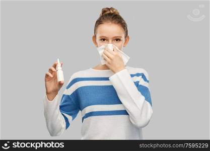 health, rhinitis and people concept - sick teenage girl blowing runny nose with paper tissue and using nasal spray over grey background. sick teenage girl with nasal spray blowing nose
