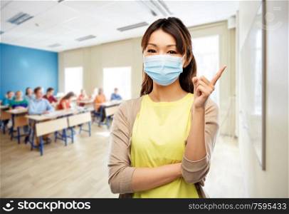 health, safety and pandemic concept - asian young woman wearing protective medical mask for protection from virus disease over school class background. asian young woman in protective medical mask