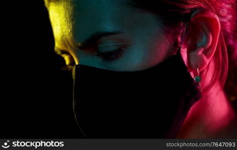health, safety and pandemic concept - close up of sad young woman wearing reusable protective mask over black background. young woman wearing reusable protective mask