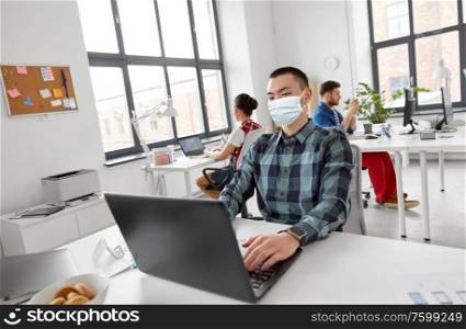 health, safety and pandemic concept - creative man wearing protective medical mask for protection from virus with laptop computer working at office. man in medical mask with laptop working at office