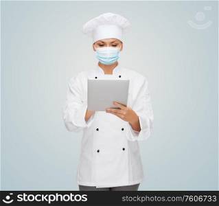 health, safety and pandemic concept - female chef, cook or baker wearing face protective medical mask for protection from virus disease with tablet pc computer. female chef in face mask with tablet pc computer