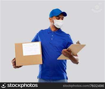 health, safety and pandemic concept - happy indian delivery man wearing face protective medical mask for protection from virus disease with parcel box and clipboard in uniform over grey background. delivery man in mask with parcel box and clipboard