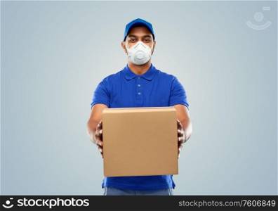 health, safety and pandemic concept - happy indian delivery man wearing face protective mask or respirator for protection from virus disease with parcel box in blue uniform over grey background. indian delivery man with parcel box in respirator