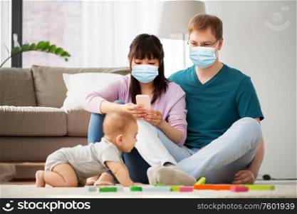 health, safety and pandemic concept - happy mother and father with baby wearing protective medical mask for protection from virus disease at home. family with baby in medical masks at home