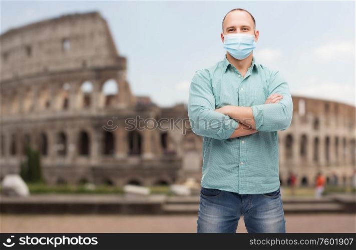 health, safety and pandemic concept - man with crossed arms wearing protective medical mask for protection from virus disease over coliseum in rome, italy background. man wearing protective medical mask in italy