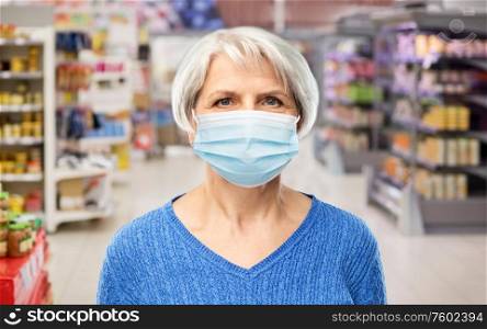 health, safety and pandemic concept - portrait of senior woman in glasses wearing protective medical mask for protection from virus over supermarket background. senior woman in medical mask at supermarket