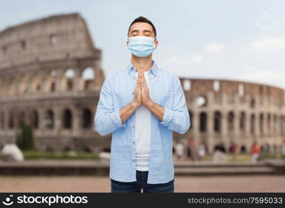 health, safety and pandemic concept - praying man wearing protective medical mask for protection from virus disease over coliseum in rome, italy background. praying man wearing medical mask in italy