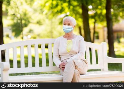 health, safety and pandemic concept - sad senior woman wearing protective medical mask for protection from virus sitting on bench at summer park. senior woman in protective medical mask at park