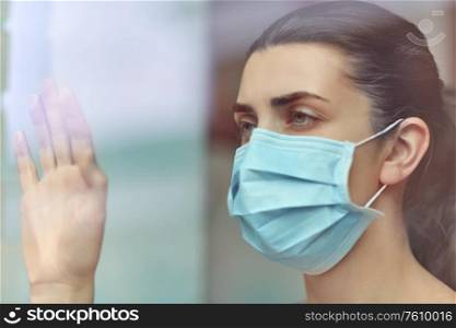 health, safety and pandemic concept - sick young woman wearing protective medical mask looking through window at home. sick young woman wearing protective medical mask