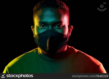 health, safety and pandemic concept - young african american man wearing reusable protective mask over black background. african american man wearing black reusable mask
