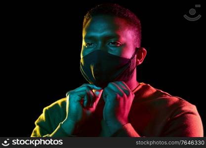 health, safety and pandemic concept - young african american man wearing reusable protective mask over black background. african american man wearing black reusable mask