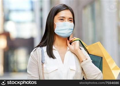 health, safety and pandemic concept - young asian woman wearing protective medical mask for protection from virus disease with shopping bags in city. asian woman in protective mask with shopping bags