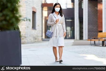 health, safety and pandemic concept - young asian woman wearing protective medical mask for protection from virus disease walking along city street. asian woman in protective medical mask in city