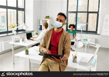 health, safety and pandemic concept - young indian man with laptop computer wearing protective medical mask for protection from virus disease working at office. indian man with tablet pc in face mask at office