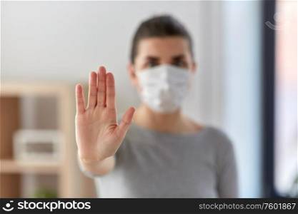 health, safety and pandemic concept - young woman in protective medical mask making stop gesture at home. woman in protective medical mask making stop sign