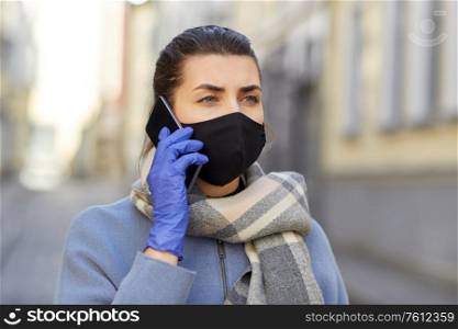 health, safety and pandemic concept - young woman wearing black face protective reusable barrier mask outdoors calling on smartphone. woman in protective reusable mask calling on phone
