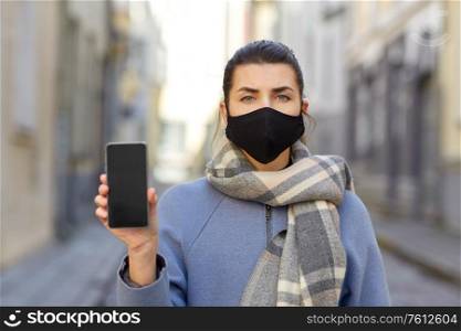 health, safety and pandemic concept - young woman wearing black face protective reusable barrier mask with smartphone outdoors. woman wearing protective reusable barrier mask