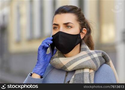 health, safety and pandemic concept - young woman wearing black face protective reusable barrier mask outdoors calling on smartphone. woman in protective reusable mask calling on phone