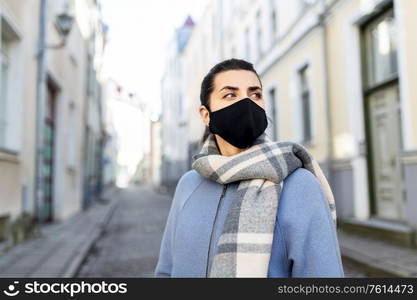 health, safety and pandemic concept - young woman wearing black face protective reusable barrier mask in city. woman wearing protective reusable mask in city