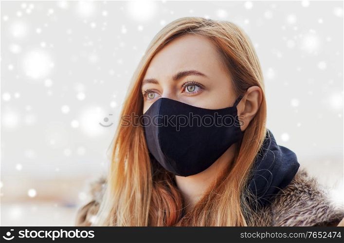 health, safety and pandemic concept - young woman wearing black face protective reusable barrier mask outdoors in winter over snow. woman wearing protective reusable barrier mask