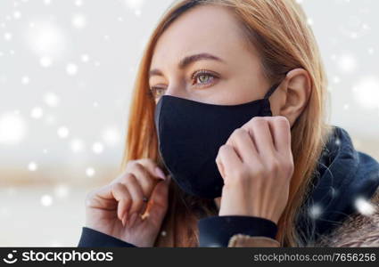 health, safety and pandemic concept - young woman wearing black face protective reusable barrier mask outdoors over snow. woman wearing protective reusable barrier mask