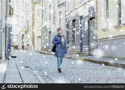 health, safety and pandemic concept - young woman wearing protective medical mask on empty street of old town in tallinn city over snow. young woman wearing protective medical mask