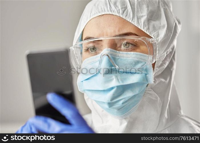 health safety, medicine and pandemic concept - close up of female doctor or scientist in protective wear, medical mask, gloves and goggles for protection from virus disease with smartphone. doctor in protective wear with smartphone