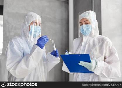 health safety, medicine and pandemic concept - female doctors or scientists in protective wear, medical masks, gloves and face shields with clipboard, test tube and cotton swab. doctors in medical mask and shield with clipboard
