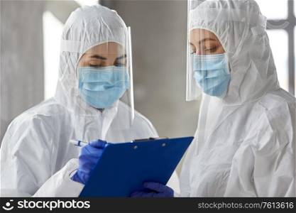 health safety, medicine and pandemic concept - female doctors or scientists in protective wear, medical masks, gloves and face shields for protection from virus disease with clipboard. doctors in medical mask and shield with clipboard
