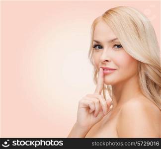 health, secret, people and beauty concept - clean face of beautiful young woman pointing finger to her lips over pink background
