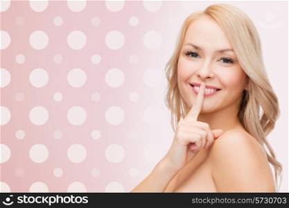 health, secret, people and beauty concept - clean face of beautiful young woman pointing finger to her lips over pink and white polka dots pattern background