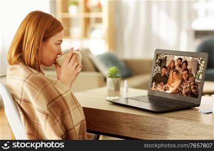 health, social distancing and technology concept - sick young woman having video call with her friends on laptop computer and drinking tea at home on christmas. sick woman having video call with friends at home
