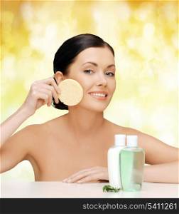 health, spa and beauty concept - smiling woman with sponge and cosmetic bottles