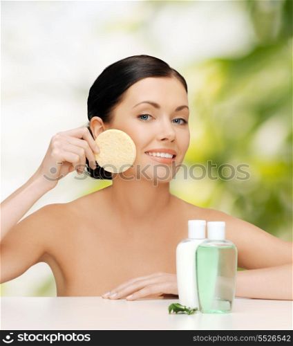 health, spa and beauty concept - smiling woman with sponge and cosmetic bottles