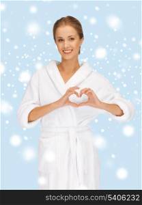 health, spa, beauty and happiness concept - beautiful woman in white bathrobe with heart shaped hands