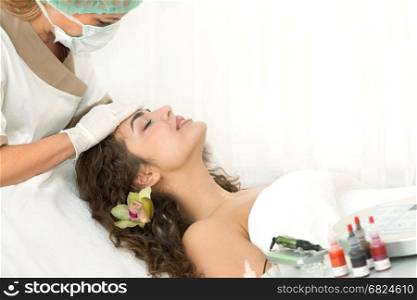 Health spa: close-up of beautiful relaxing young woman having facial massage (electrolysis), with orchid in long brown hair.