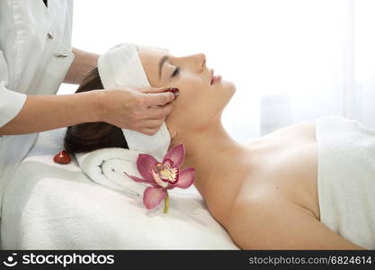 Health spa: close-up of beautiful relaxing young woman having facial massage (electrolysis), with orchid in long brown hair.