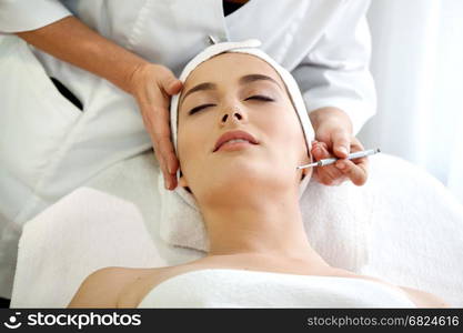 Health spa: close-up of beautiful relaxing young woman having facial massage (electrolysis), with orchid in long brown hair.