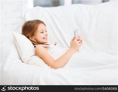 health, technology and beauty concept - little girl with smartphone playing in bed