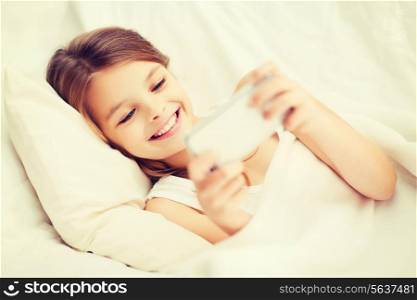 health, technology and beauty concept - little girl with smartphone playing in bed
