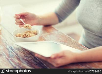 health, technology, internet, food and home concept - close up of woman eating porridge and using tablet pc computer
