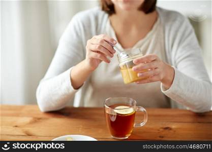 health, traditional medicine and ethnoscience concept - close up of ill woman drinking tea with lemon and honey at wooden table